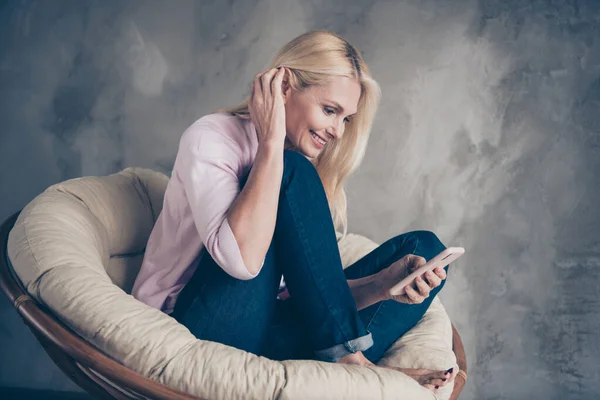 Portrét pozitivní veselý středního věku žena použít její smartphone typ příspěvek komentář na účet sociálních médií sedět v měkké bílé proutěné křeslo bosá v obývacím pokoji uvnitř — Stock fotografie