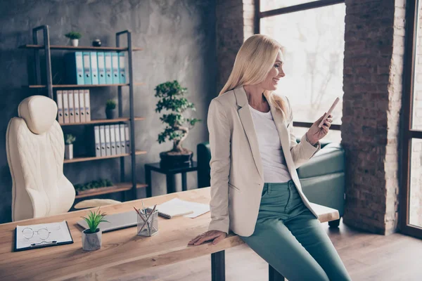 Retrato de seguro positivo cabello rubio fresco de mediana edad empresaria utilizar sus mensajes de tipo de teléfono celular comunicarse chat con socios de trabajo los inversores se sientan en la mesa de madera en el lugar de trabajo de la oficina — Foto de Stock