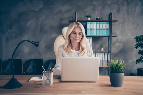 Foto da velha mulher de cabelos brancos trabalhando com seu laptop on-line com seus colegas de trabalho usando a tecnologia moderna para se comunicar com a equipe corporativa — Fotografia de Stock
