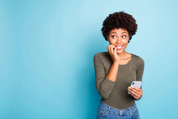 Portrait of scared emotions expression mulatto girl use cellphone have social media trouble failure send sms by mistake panic nail bite look wear green trendy pullover isolated blue color background