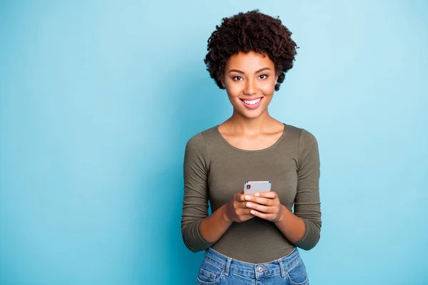 Portret van positieve vrolijke donkere huid meisje gebruik houden haar smartphone genieten blog posts opmerkingen dragen groene outfit geïsoleerd over blauwe kleur achtergrond — Stockfoto