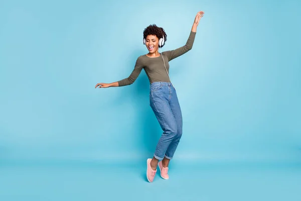 Foto de corpo inteiro de alegre engraçado mulato menina tem tempo livre ouvir música em seu fone de ouvido dança cantar desfrutar de desgaste elegante verde pulôver jeans sapatilhas isoladas sobre fundo de cor azul — Fotografia de Stock