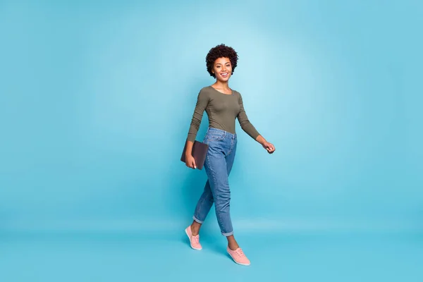 Teljes méretű fotó pozitív magabiztos független hűvös sötét bőr lány szabadúszó megy sétálni a munkát a cég tartsa neki netbook viselni alkalmi stílusú ruhák rózsaszín tornacipő elszigetelt kék színű háttér — Stock Fotó