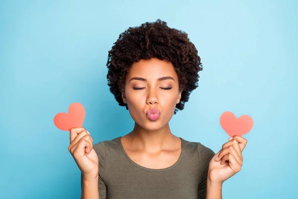 De cerca la foto de la chica de piel oscura coqueta de ensueño sostiene poco corazón de tarjeta de papel rojo para 14-febrero tienen fecha con el novio enviar aire beso desgaste jersey verde de moda aislado sobre fondo de color azul — Foto de Stock