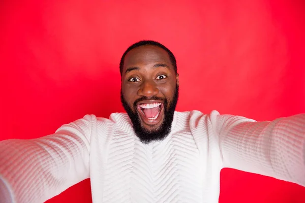 Zdravím, drazí následovníci. Fotografie legrační tmavé kůže muž drží telefon dělat bezstarostné selfie nosit bílý pletený svetr izolované červené pozadí — Stock fotografie