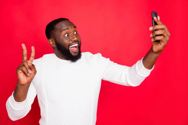 Merhaba sevgili takipçiler. Elinde telefon tutan komik, koyu tenli bir adamın, V işaretini gösteren selfie çekerken beyaz örülmüş süveter giydiği fotoğraf. — Stok fotoğraf