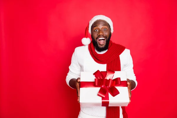 Wow es für mich. Porträt des aufgeregten afrikanischen Mannes in Weihnachtsmannmütze halten großes Paket erhalten Geschenk für Neujahrsparty von seinem Freund tragen Stil Pullover isoliert über rotem Hintergrund — Stockfoto