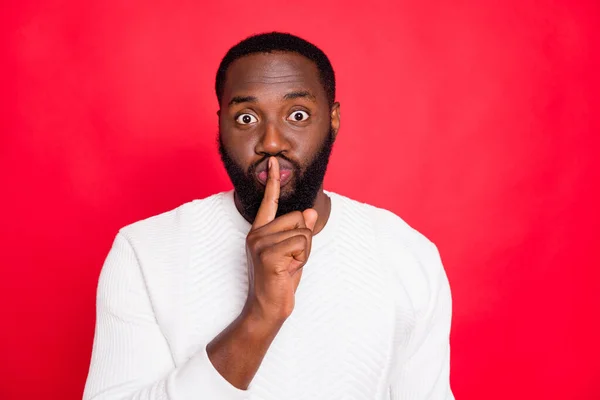 Portret funky sprytny afrykański mulat człowiek pokazać palec wskazujący w pobliżu jego usta twarz zapytać nie dzielić prywatne informacje nosić styl biały sweter izolowany na czerwonym tle kolor — Zdjęcie stockowe
