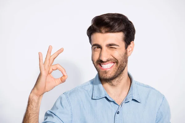 Foto von netten multiethnischen gutaussehenden Kerl zeigt okey Symbol Genehmigung gute Qualität des Produkts zwinkernden Augen tragen lässig Jeanshemd isoliert weißen Farbhintergrund — Stockfoto