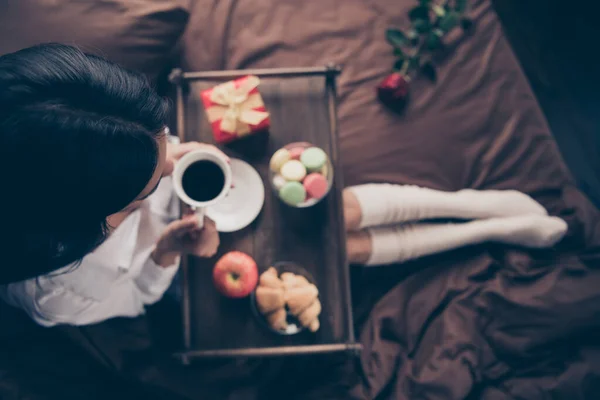 멋진 아가씨가 긴 다리를 하고 침대에 앉아 커피를 마시며 리넨 베틀 위에서 맛있는 집에서 구운 스낵을 먹고 있는 모습 이 높은 각도로 바라본 모습 — 스톡 사진