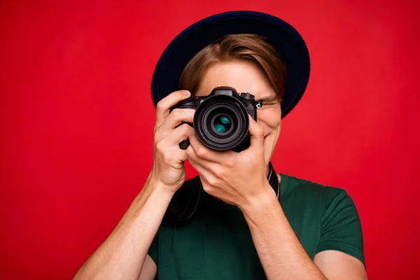 De cerca la foto del turista alegre chico positivo en el extranjero visita excursión divertirse tomando fotos con su cámara dlsr desgaste azul terciopelo gorra de la cabeza verde camiseta aislada sobre fondo de color rojo — Foto de Stock