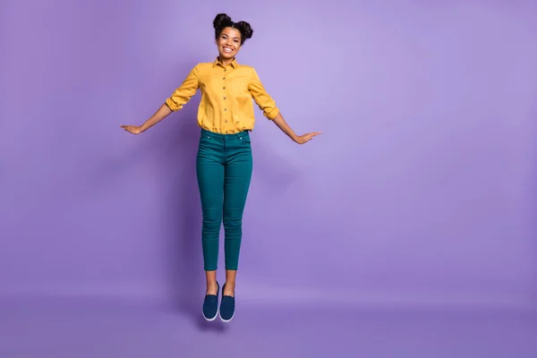 Foto de comprimento total de senhora de pele muito escura pulando alto paquetes humor coquete férias tempo desgaste casual camisa amarela calças isoladas cor roxa fundo — Fotografia de Stock