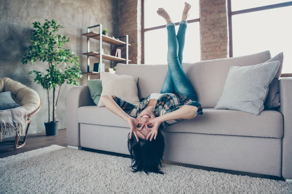 Foto de tamaño completo de la señora divertida regocijándose levantando las piernas al revés mostrando símbolos okey cerca de ojos especificaciones forma sofá acostado desgaste ropa casual apartamento interior — Foto de Stock