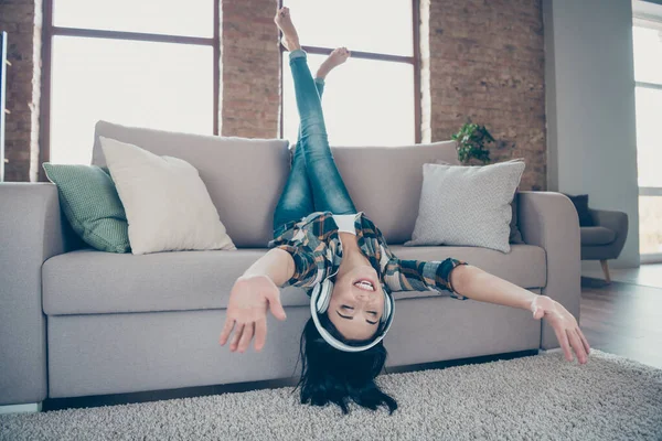 Full size photo of funny lady rejoicing listening favorite radio fm in modern earflaps raising legs upside down lying sofa wear casual clothes apartment indoors — Stock Photo, Image