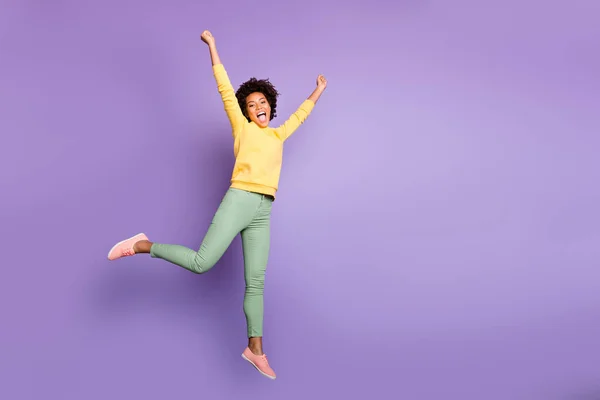 Full length photo of delighted crazy mulatto girl win fall autumn jackpot sales discounts jump raise fists scream yeah wear yellow pullover green pants trousers isolated over purple color background — Stockfoto