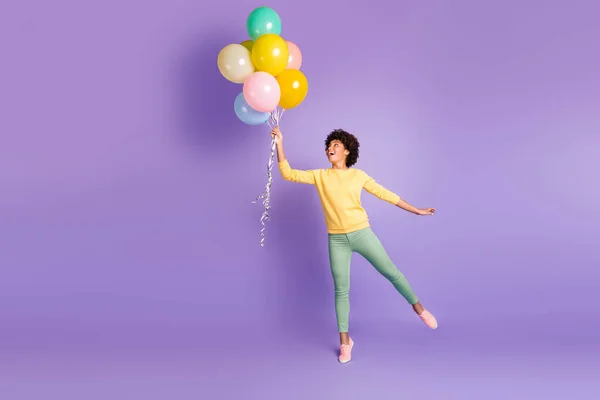 Full length profile side photo of amazed funky funny dark skin girl hold many baloons think she can fly in the sky enjoy rejoice wear trendy green sweater outfit isolated over violet color background — 스톡 사진