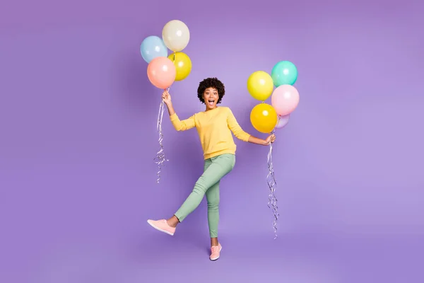Full size photo of funky funny teen mulatto girl hols many colorful baloons feel content crazy on spring holidays wear green sweater green pants trousers isolated over violet purple color background — Φωτογραφία Αρχείου
