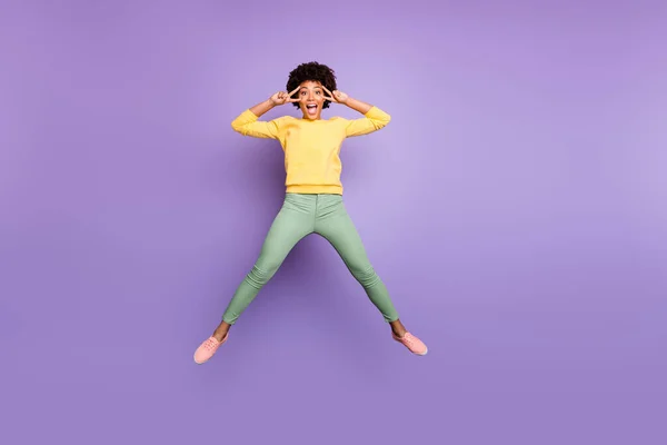 Foto de corpo inteiro de espantado despreocupado afro americano menina salto divirta-se no outono primavera feriados fazer v-sinais desgaste amarelo pulôver verde calças calças isoladas sobre violeta roxo cor fundo — Fotografia de Stock