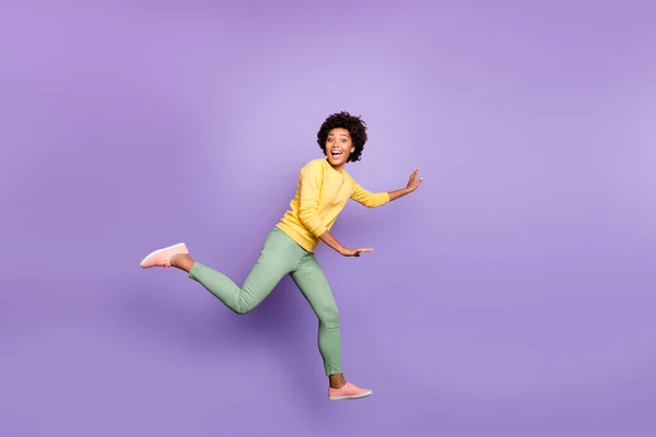 Полноразмерная фотография профиля бодрой возбужденной волосатой девочки-мулатки прыгать играть в догонялки с друзьями по весне носить желтые пуловер зеленые брюки изолированный фиолетовый фон — стоковое фото