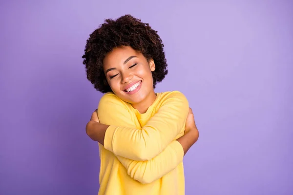 照片上是迷人的、甜美的、漂亮的小女孩，她笑着抱着自己，享受着她新买的黄色毛衣，这件毛衣很舒适，背景是淡紫色的 — 图库照片