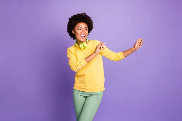 Foto de rizado ondulado alegre bailarina funky positivo con pantalones verdes pantalones que se enfría con auriculares en aislado sobre fondo de color pastel púrpura — Foto de Stock