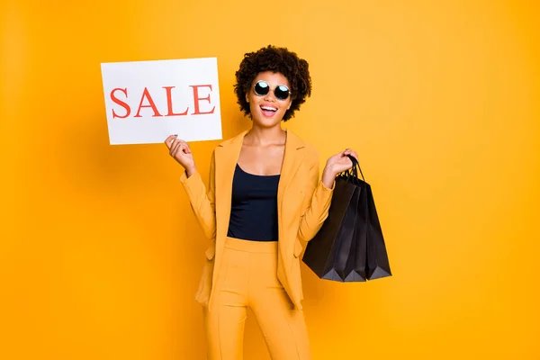 Portret van funky positieve vrolijke dame houden zwarte tassen genieten van zwarte vrijdag verkoop op vrije tijd wilt winkelen kleding stijl broek broek geïsoleerd over gele kleur achtergrond — Stockfoto
