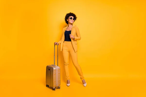 Foto em tamanho completo de positivo alegre menina segurar trole pacote pronto para desfrutar de tempo livre em férias desgaste elegante moda roupa calças calçado isolado sobre cor amarela fundo — Fotografia de Stock