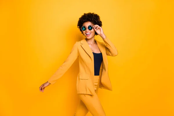 Профільна бічна фотографія чарівної позитивної веселої темної шкіри леді торкається її окулярів мають вільний час іти пішки носити стильний одяг ізольовані на жовтому яскравому кольоровому фоні — стокове фото