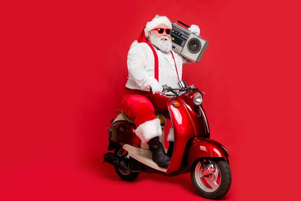 Portrét pěkné vousaté veselý tuk velké břicho funky Santa hipster na sobě festal čepice klobouk čelenky na koni motor kolo nesoucí boombox izolované na jasné živé lesk pulzující červené barvy pozadí — Stock fotografie