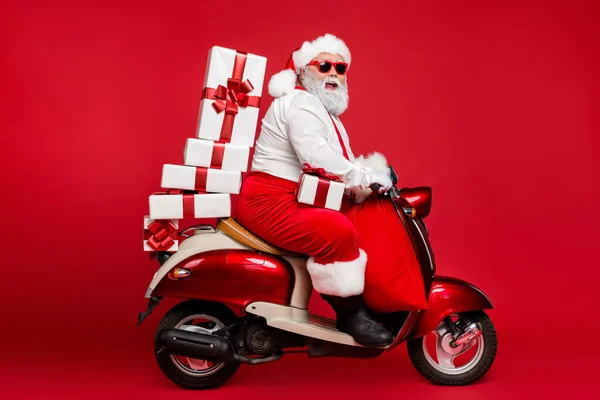 Güzel sakallı, neşeli, neşeli, eğlenceli Noel Baba 'nın profiline bakın. Moped' e binmiş, yığınla peri alışverişi yapıyor. Parlak, parlak, parlak, kırmızı bir arka planda izole edilmiş alışveriş indirimi yapıyor. — Stok fotoğraf