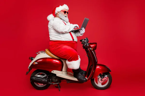 Güzel sakallı, koca göbekli Noel Baba elinde dizüstü bilgisayarla oturmuş dilek listesi e-postalarını okuyor. Kış perisi parlak parlak kırmızı arka planda izole edilmiş. — Stok fotoğraf