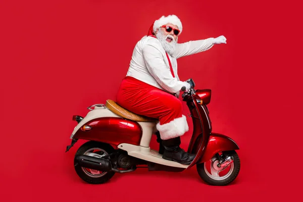 Profil side view portret ładny brodaty wesoły śmieszne funky celowe Santa Claus jazdy motorower pośpiech się zakupy sezon Biegun Północny izolowane na jasny żywy połysk żywy czerwony kolor tło — Zdjęcie stockowe