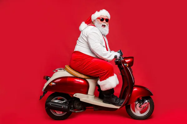 Profile side view portrait of nice bearded cheerful cheery funny Santa father riding motor bike having fun shopping winter season isolated on bright vivid shine vibrant red color background — Stock Photo, Image