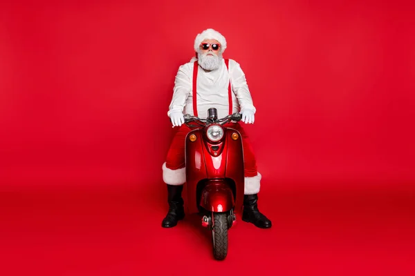 Porträt von seinem schönen attraktiven bärtigen ernsthaften Weihnachtsmann, der auf einem Motorrad sitzt und Bestellungen ausliefert Winter isoliert über hellem, lebendigem Glanz leuchtend roten Hintergrund — Stockfoto