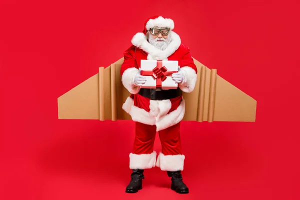 Full length photo of cool funky αεροπόρος santa claus in cap hat give craft package to kids in christmas night wear belt pants isolated over red background — Φωτογραφία Αρχείου