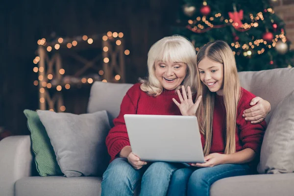 Portrait of nice attractive lovely glad cheerful cheery granny pre-teen grandchild using laptop making video calls waving hi hello festal atmosphere at decorated industrial loft style interior house — ストック写真
