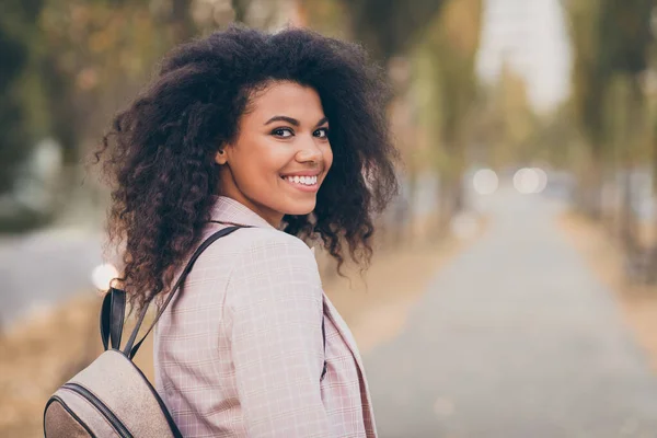 Photo of charming pretty dark skin curly lady walking park after college lectures hold backpack waiting friend join company autumn season wear jacket outdoors — Zdjęcie stockowe
