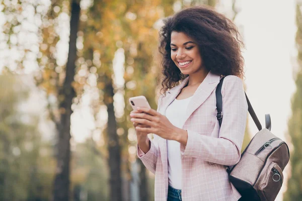 Foto van mooie duizendjarige donkere huid golvende dame lopen park na lezingen houden telefoon lezen nieuws genieten warme herfst weer dragen tas jeans buiten — Stockfoto