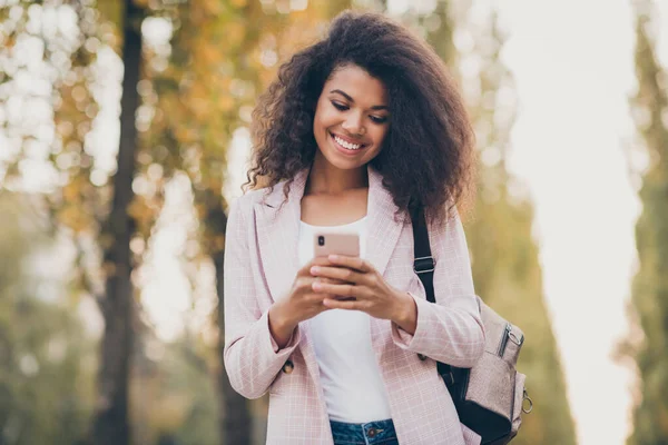 Photo of amazing pretty dark skin lady spend free time walk park after university lectures hold phone reading hírek őszi viselet kabát farmer szabadban — Stock Fotó