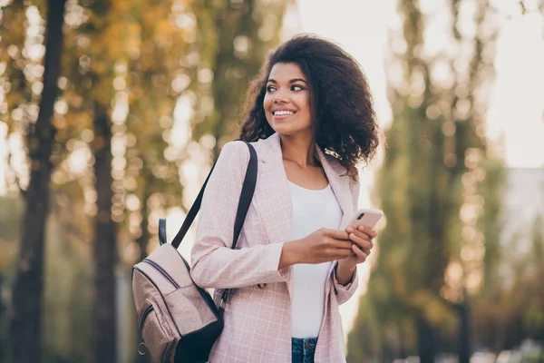 Foto van verbazingwekkende vrij donkere huid dame besteden vrije tijd wandelen park na de universiteit lezingen houden telefoon rugzak herfst dragen jas jeans buiten — Stockfoto