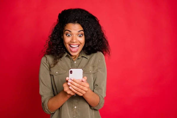 Foto de pelo castaño alegre excitado alegre novia gritando navegar a través de su teléfono encontrar un montón de noticias frescas aislados en la camisa sobre fondo de color vivo rojo — Foto de Stock