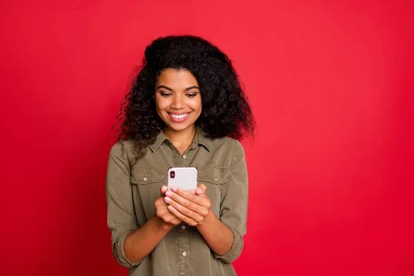 Foto de alegre positivo lindo bastante agradable joven navegando a través de su teléfono inteligente en busca de nueva información sonriente aislado fondo de color rojo vivo — Foto de Stock