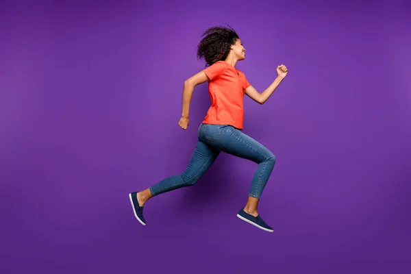 Full length body size φωτογραφία του χαρούμενα χαριτωμένο αρκετά θετική φίλη σγουρά κυματιστό τρέξιμο προς τα ψώνια φορώντας τζιν τζιν τζιν πορτοκαλί t-shirt απομονωμένο ζωντανό χρώμα βιολετί φόντο — Φωτογραφία Αρχείου