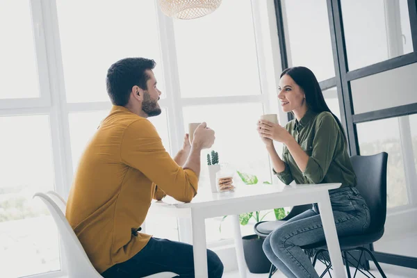 Profile photo of handsome guy and his pretty lady looking tender eyes drinking hot beverage sitting chairs opposite in stylish interior light cafeteria indoors wear casual clothes — Stock Photo, Image
