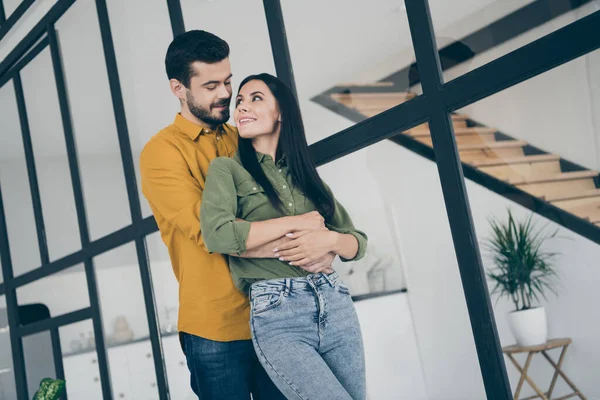 Foto de chico guapo y su esposa dama mirando tiernos ojos moviéndose para alquilar piso casado personas abrazando a cuestas en el interior moderno piso interior usar ropa casual —  Fotos de Stock