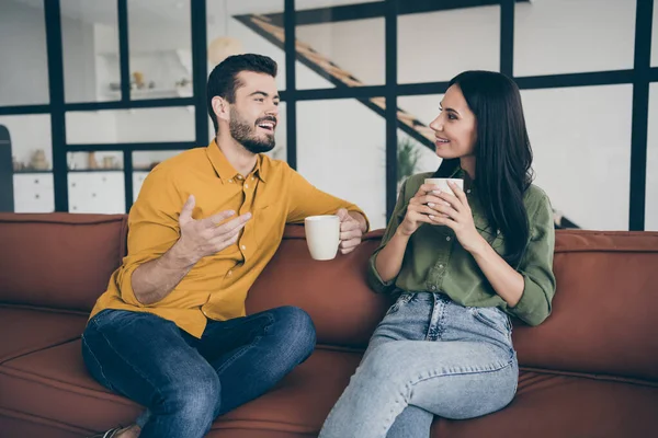 Photo of funny guy and lady having fun best weekend sharing fresh news drinking hot beverage sit sofa in modern style interior flat indoors wear casual clothes — Stock Photo, Image