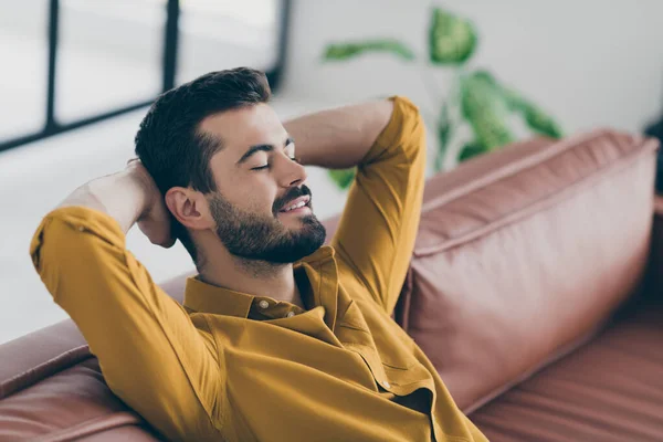 Foto de un chico guapo de buen humor cogido de la mano detrás de la cabeza ojos cerrados sentado sofá de la oficina pequeño descanso de café en el espacio de trabajo moderno en el interior — Foto de Stock