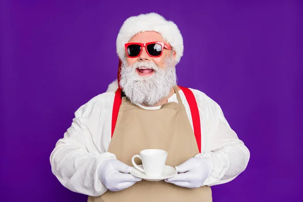 Крупным планом портрет милой веселой веселой бородатой Санта-баристы, держащей в руках чашку эспрессо, изолированную на ярком ярком фиолетовом фоне — стоковое фото