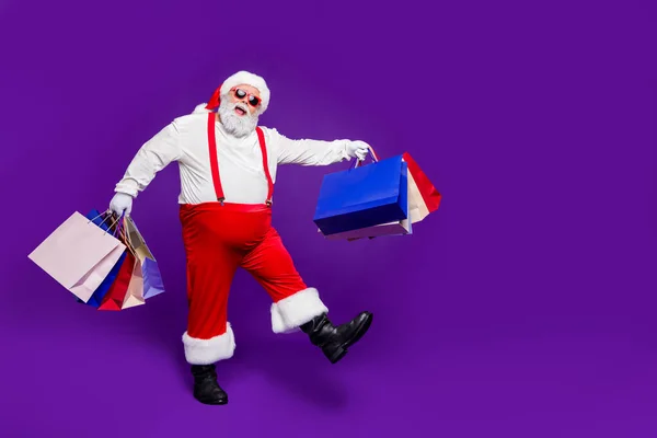 Full length body size view of his he nice carefree funky glad cheerful positive bearded thick fat Santa carrying bags new clothes walking isolated on bright vivid shine vibrant violet lilac background — Stok fotoğraf