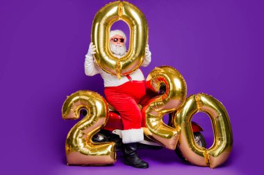 Full body photo of fat santa man sitting on bike holding big air newyear 2020 numbers balloons congratulating people wear sun specs x-mas costume isolated purple background clipart